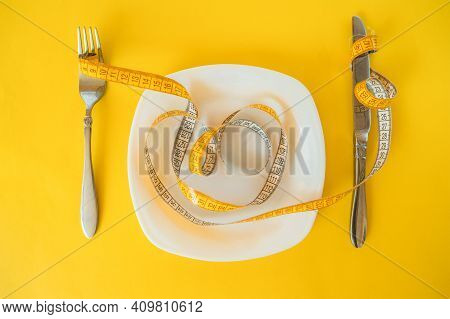 Measuring Tape On Fork And Plate And Knife On A Yellow Background. Body Weight Loss Concept.