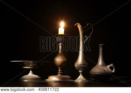Set Of Vintage Dishes Near Lighting Candle On Dark Background
