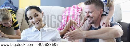 Man And Woman And Their Children Are Smiling And Laughing While Sitting On Floor And Looking At Lapt