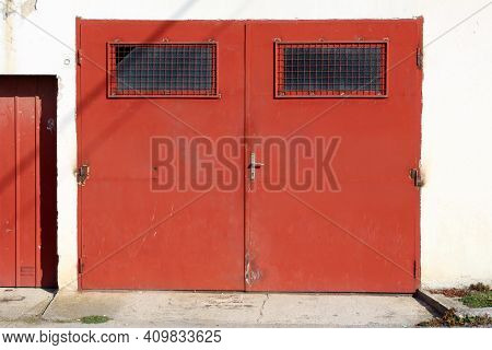 Strong Old Dark Red Metal Garage Doors With Rusted Hinges And Windows Covered With Metal Protection 