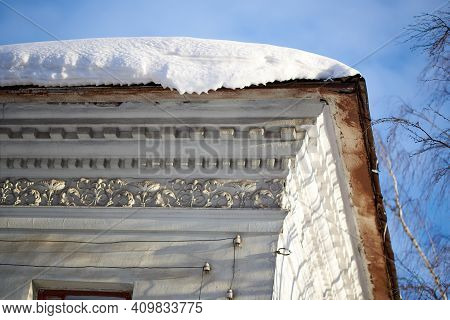 A Snowdrift Hanging From The Roof Of An Old House. Weather Anomaly, Abnormally Cold Winter