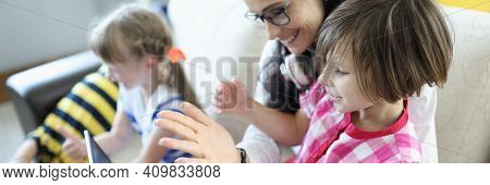 Woman Is Sitting On The Couch, Girl Is Sitting On Her Lap, They Are Looking At Laptop Next To Childr