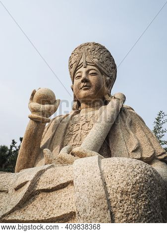 Qingdao, China - December 2017: White Carved Buddhist Sculpture Holding A Ball And Scroll At The Ent