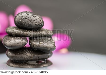 Spa Stone Tower In A Milky Liquid With A Blurred Purple Orchid In The Background Against A Dark Back