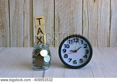 Tax Text On Wooden Block Cube On Top Of Glass Jar With Multicurrency Coins And Alarm Clock. Tax Time