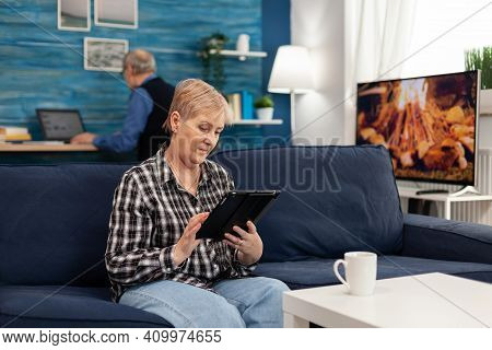 Senior Lady Scrolling On Digital Device Relaxing On Sofa. Elderly Woman Using Moder Technoloy Tablet