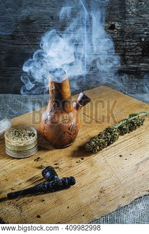 Old Brown Steamung Bong And Open Cannabis Grinder With Chopped Marijuana Weed And Medical Cannabis I