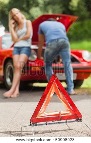 Close up on triangle warning sign with broken down car on background