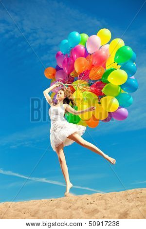 Beautiful young stylish woman with ainbow balloons in hands against the sky. Positive girl on nature. Smiling woman outdoors enjoying.