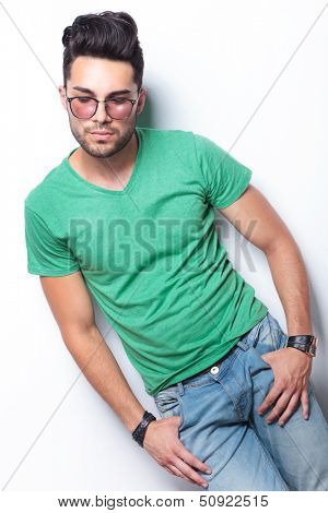 young casual man holding both thumbs in front pockets and looking down, away from the camera. on white background