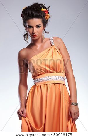young fashion woman holding her dress with both hands and looking into the camera with a serious expression. on gray background