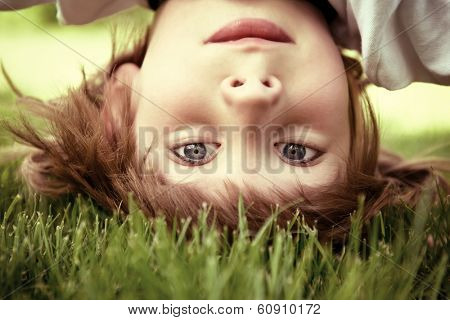 Happy little boy standing upside down on green grass in spring park, toned