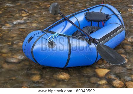 a blue packraft (one-person light raft used for expedition or adventure racing) with a kayak paddle against a shallow river