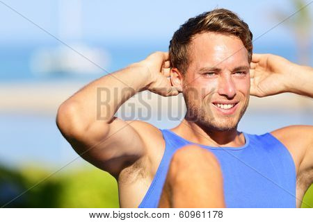 Fitness man doing sit-ups outdoor. Close up portrait of male fitness model training sit up exercise during outside workout in grass in summer. Handsome muscular male sport model working out.