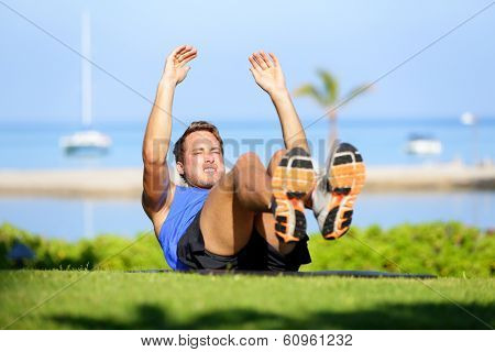 Fitness man doing sit-ups exercise for abs outdoors. Fit male athlete cross training jackknife sit up during workout. Muscular handsome young caucasian man working out outside.
