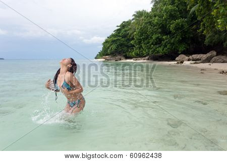 Happy carefree Asian woman in a bikini playing in the sea splashing herself with water as she enjoys cooling off in the hot summer sunshine