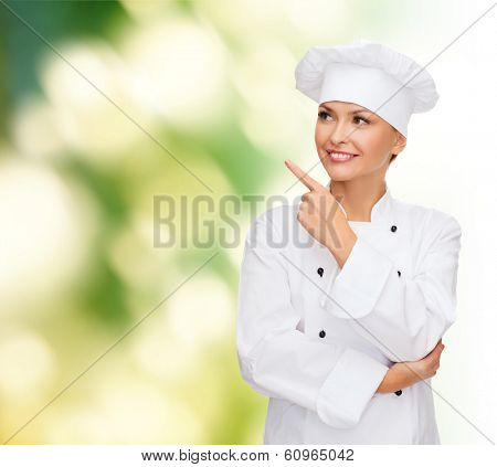 cooking, advertisement and food concept - smiling female chef, cook or baker pointing finger to something