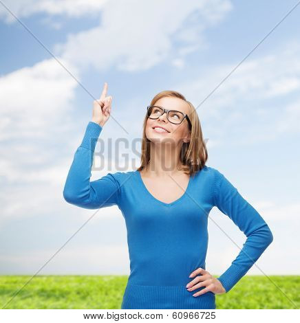 advertisement concept - attractive young woman in casual clothes and black eyeglasses pointing her finger up