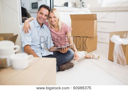 Portrait of a smiling couple using digital tablet amid boxes in a new house
