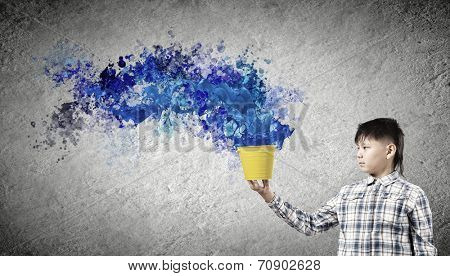 Young boy splashing colorful paint from bucket