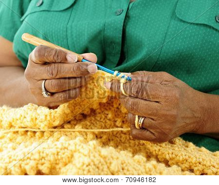 Close-up image of a senior woman's hands crocheting a gold-colored afghan.  