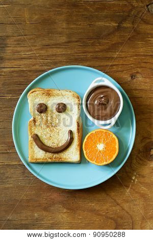 breakfast serving funny face on the plate (toast, chocolate spread and orange)