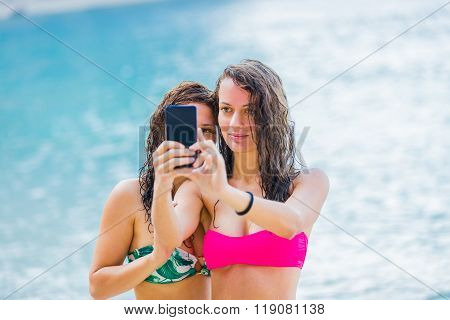 Young girls photographing themselves on the beach with a black smartphone.