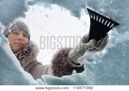Woman Cleaning Window Of Car From The Snow With Scraper