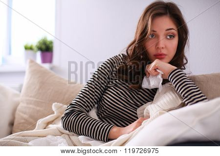 Portrait of a sick woman blowing her nose while sitting on the sofa
