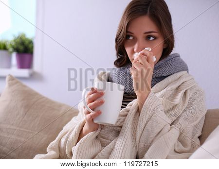 Portrait of a sick woman blowing her nose while sitting on the sofa