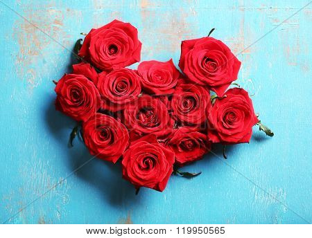 Fresh red roses buds in shape of heart on blue wooden background