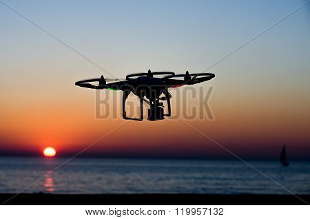Flying drone with camera on the sky at sunset