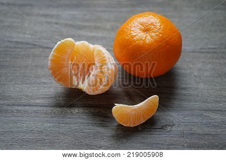 peeled and unpeeled clementines or mandarin oranges on rustic wooden board with shallow depth of field