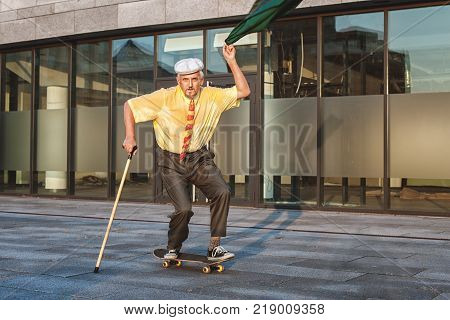Playful grandfather is rolling on a skateboard in his hand a jacket with which he is waving.