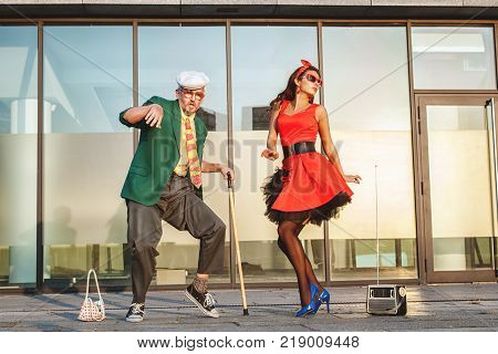 Grandfather dances there is a walking-stick in his hands a young woman is dancing next.