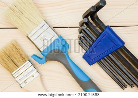 A set of repair tools- paint brushes and hex keys on a light uncolored wooden background. Close up. Top view. Space for your text or pruduct display.