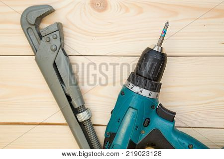 Repairing and construction concept. A screw gun and pilers on a light uncolored wooden background, close up. Top view. Space for your text or pruduct display.