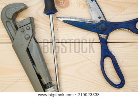 Repairing and construction concept. A set of tools for house repair- scissors, screwdriver and pilers on a light uncolored wooden background, close up. Top view. Space for your text or pruduct display.