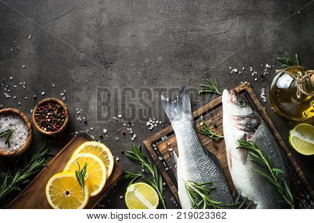 Fresh fish seabass and ingredients for cooking. Raw fish seabass with spices and herbs on black slate background. Top view with copy space.