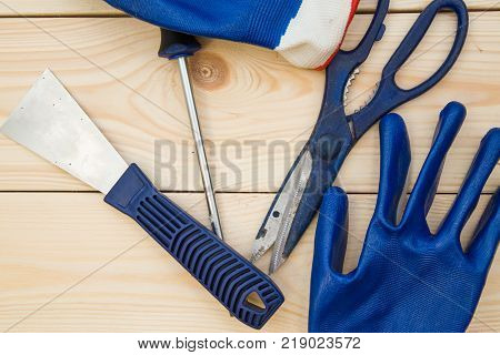 Repairing and construction concept. A set of tools -a plastering trowel, scissors, screwdriver and gloves on a light uncolored wooden background, close up. Top view. Space for your text or pruduct display.