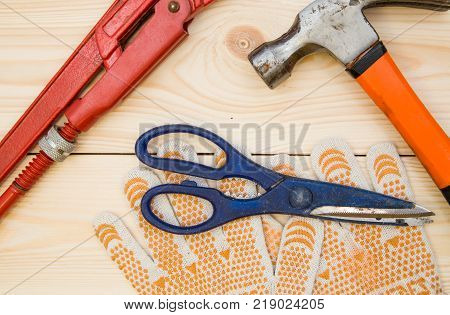 Repairing and construction concept. Tools for house repair- hammer, scissiors and a pair of protective work gloves on a light uncolored wooden background, close up. Top view. Space for your text or pruduct display.