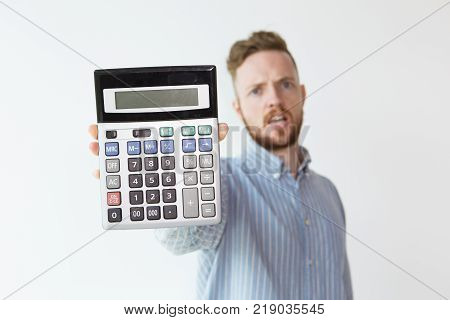 Portrait of upset young man unfocused with calculator in focus. Book-keeper demonstrating loss. Finance and disadvantage concept.