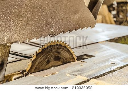 Disc electric circular saw on the stand frame. Sawing machine in working carpentry workshop. Mechanized woodworking carpenter tool close-up. Toothed saw blade. Limeted depth of field.