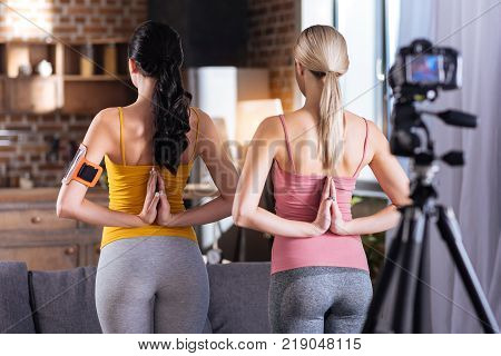 Yoga pose. Nice positive well built women tuning their back to the camera and putting their hands together while performing a yoga pose