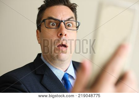 Shocked businessman reading last news on phone and not trusting his eyes. Excited middle-aged male employee in eyeglasses receiving shocked message. Astonishment concept