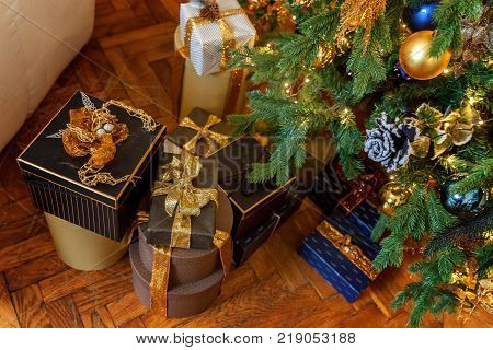 Black paper gift boxes with golden ribbon bow near the Christmas tree. Classic christmas and New Year decorated interior room with presents and New year tree.