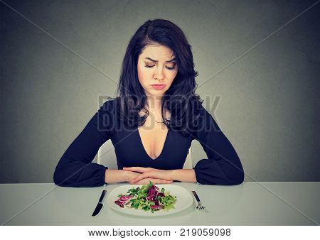 Young woman looking at plate of salad with desperate expression having diet.