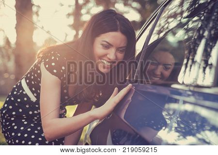 Excited young woman and her new car outdoors with sunlit forest in background.