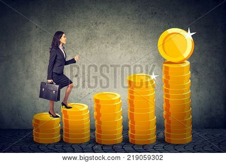 Businesswoman with briefcase stepping up a financial stairway ladder made of gold coins
