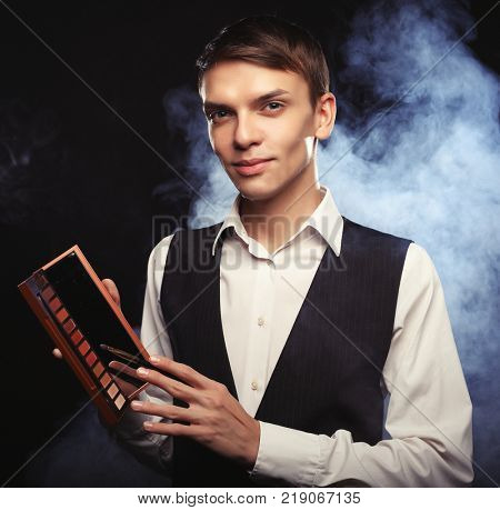 Male make-up artist  staying on dark  background, holding profes